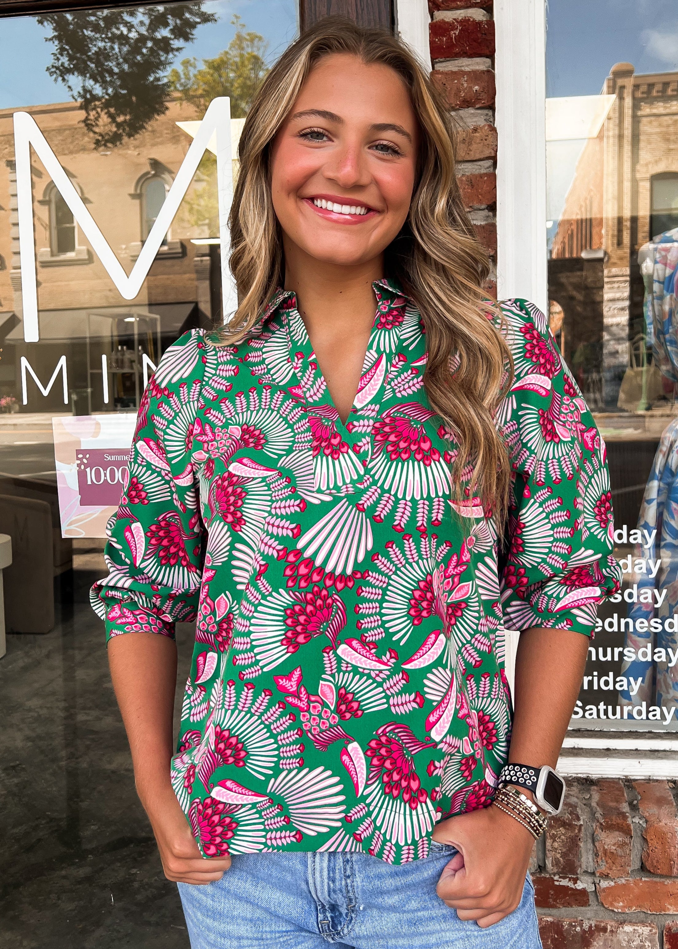 Woman in a floral shirt standing in front of a store with a glass door.
