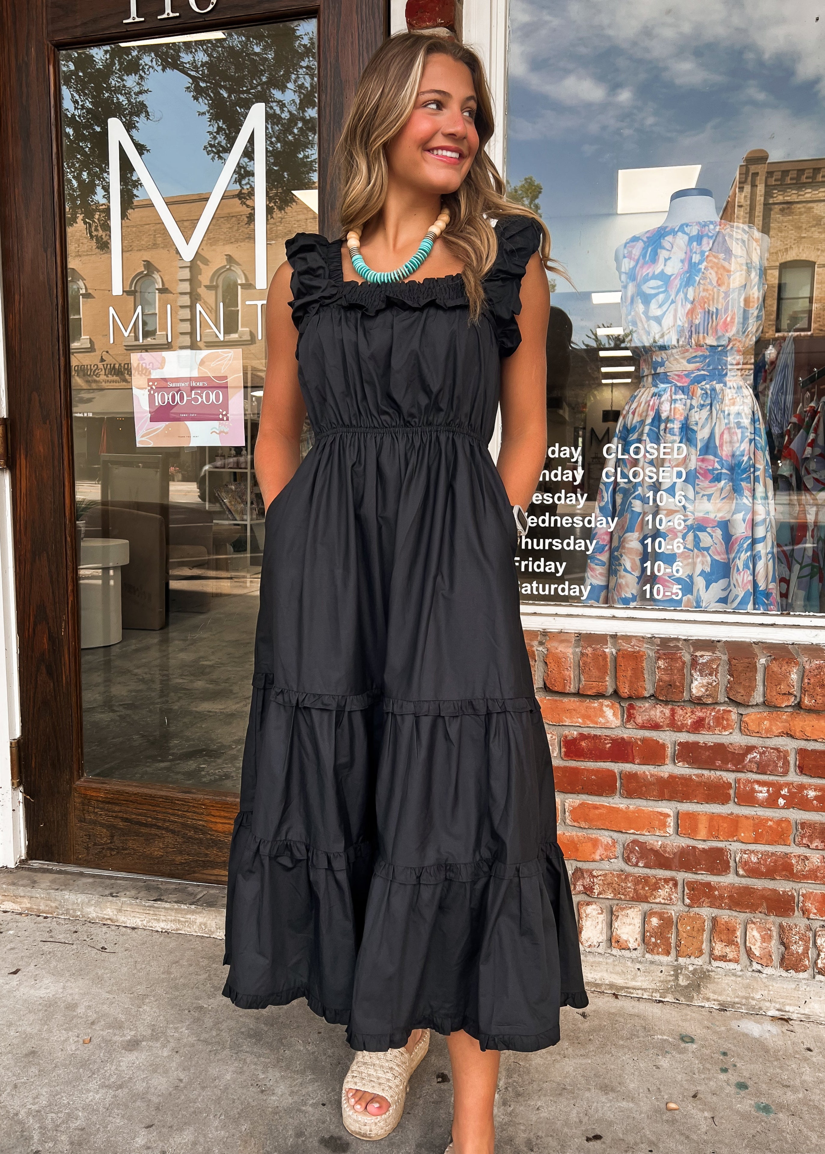 Woman in a black dress standing outside a store with a brick wall and glass door.